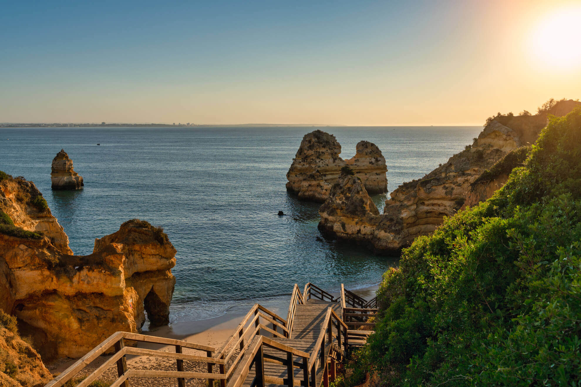 Golden morning sunlight illuminating the wooden staircase descending to Praia do Camilo beach in Lagos