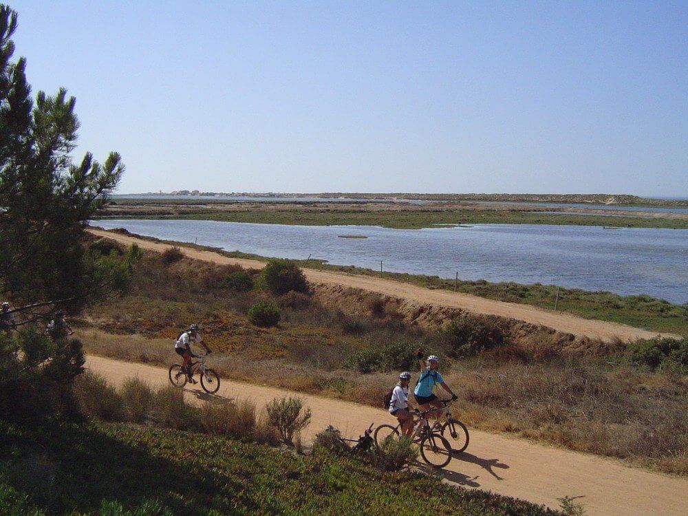 People leisurely cycling along the flat gravel paths bordering the main lagoon in Quinta do Lago